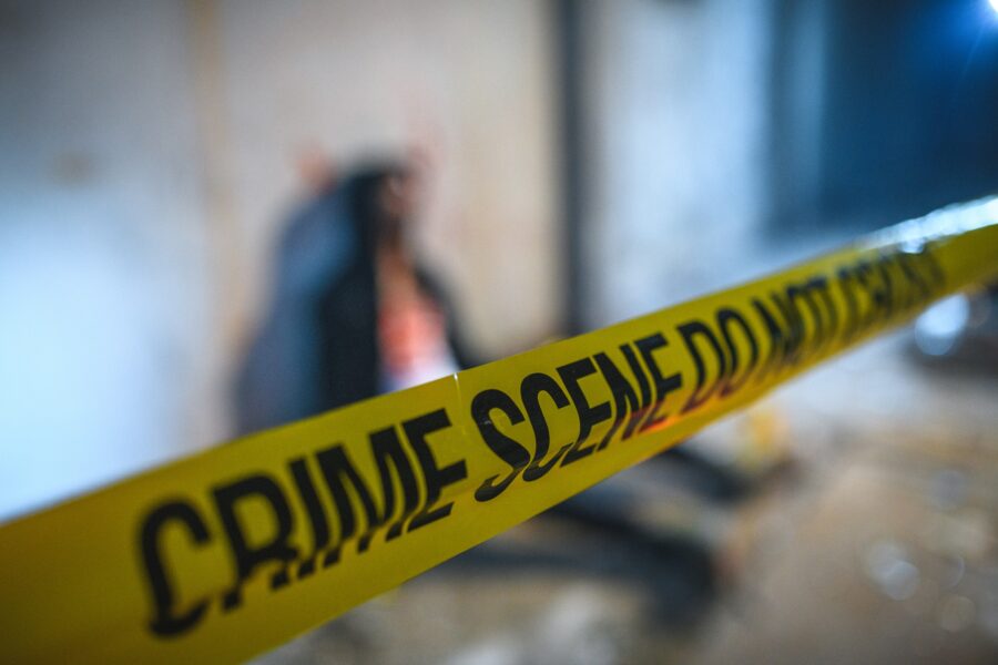 Barricade tape covering a crime scene. There is a dead male body in the background indicating homicide.