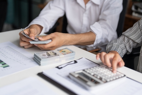 two professionals counting US dollar banknotes beside calculator and financial documents