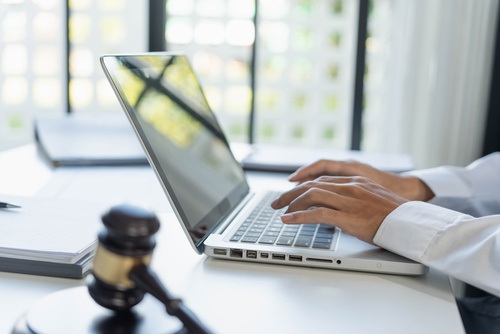 attorney typing on laptop beside gavel and legal documents on desk